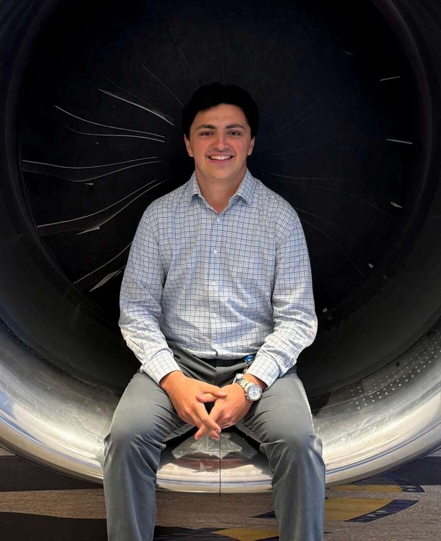 Sam Rizzo, smiling, seated in front of a jet engine display.